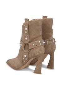 Botas de tobillo de ante en tono marrón claro con punta afilada, acentos de tachuelas y un tacón bloque alto. Cuenta con una correa decorativa y elementos metálicos.
