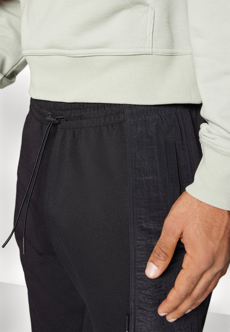 Sweatshirt vert clair avec ourlet côtelé, associé à un jogging noir avec un panneau latéral texturé et une taille ajustable à cordon.