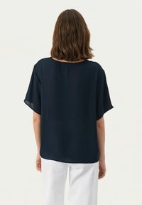 Top blu navy a maniche corte in tessuto leggero, con scollatura rotonda e vestibilità rilassata. La vista posteriore mostra una texture liscia e fluente.