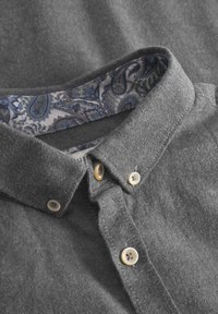 Grau gestreiftes Hemd mit strukturiertem Stoff. Der Innenkragen zeigt ein blaues Paisleymuster mit kontrastierenden Knöpfen in hellen und dunklen Farbtönen.