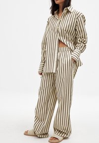 Striped cotton shirt and wide-leg pants in beige and brown, featuring a relaxed fit and an elastic waistband. Sandals with woven texture.