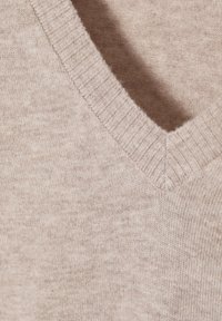 Pull beige doux à col en V montrant un col côtelé et une texture de tissu tricoté lisse.