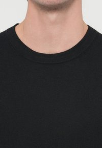 Czarny dziergany sweter z okrągłym dekoltem i gładką fakturą, widoczny od ramion w górę. Swobodny i dopasowany fason.