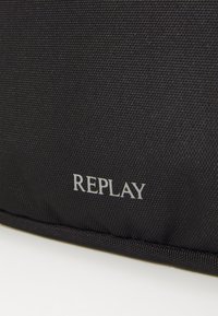 Black fabric bag featuring the embossed logo "REPLAY" in silver. Textured surface with a structured design and reinforced edges.