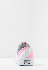 Zapatillas de lona que presentan paneles en rosa, azul y blanco, con una suela de goma blanca. En la parte trasera se muestra una etiqueta con "DIVERSIDAD IGUALDAD AMOR."