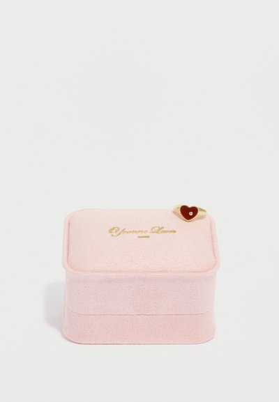 Ružová zamatová šperkovnica so zlatým nápisom. Obsahuje malý prsteň so srdcovým červeným akcentom na vrchu. Mäkký, textúrovaný materiál.