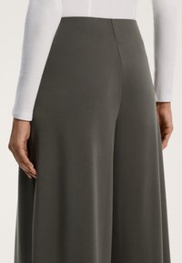 Spodnie o szerokich nogawkach w ciemnoszarym materiale, z gładką teksturą i wysokim stanem. Biała bluzka z długim rękawem częściowo widoczna na górnej części ciała.