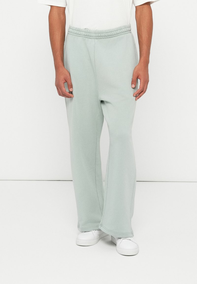 Helle grüne Sweatpants mit elastischem Bund, geraden Beinen und weichem Material, kombiniert mit weißen Sneakers.