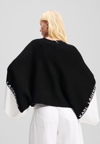 Crni oversized džemper s bijelim rukavima, s natpisom brenda "KARL LAGERFELD" u bijeloj boji na lijevom rukavu, mekan na dodir.