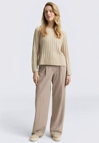 Beiger, gerippter Strickpullover mit entspannter Passform und langen Ärmeln, kombiniert mit hoch taillierten, beigen, weit geschnittenen Hosen und cremefarbenen Schuhen.