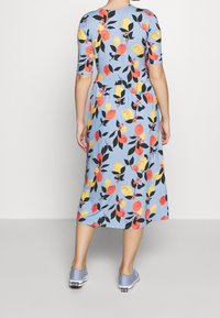 Blumen-Midi-Kleid mit einem hellblauen Hintergrund und roten, gelben und schwarzen Blumenmustern. Kurze Ärmel und geraffte Taille, kombiniert mit blauen Turnschuhen.