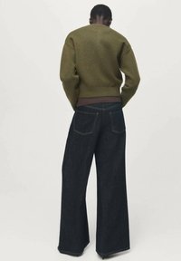 Suéter de punto verde con cuello redondo, combinado con pantalones vaqueros de pierna ancha de mezclilla oscura que cuentan con bolsillos traseros estándar y costuras en contraste.