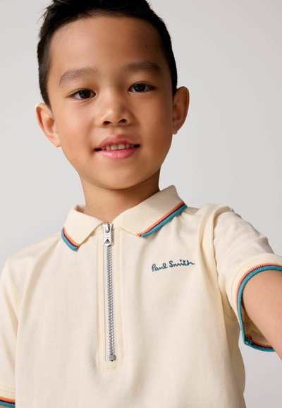 Krémové bavlnené polo tričko so zipsom na golieri. Obsahuje farebné prúžky na golieri a rukávoch, s modrým vyšitým nápisom "Paul Smith".