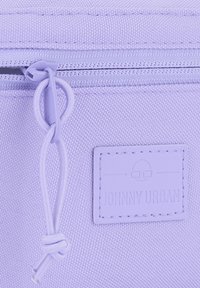 Pochette en tissu lilas avec une surface texturée, dotée d'une fermeture éclair et d'une étiquette en cuir imprimée avec un lettrage en relief.