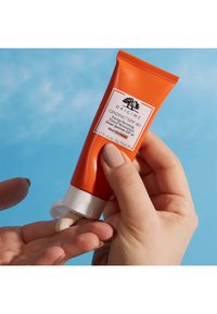Oransje tube med Origins GinZing SPF 40 fuktighetskrem, jevn krem som presses ut på hånden, designet for solbeskyttelse og fuktighet.