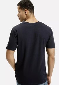 Czarna bawełniana koszulka z krótkim rękawem, okrągłym dekoltem i gładką fakturą. Widok z tyłu, prezentujący minimalny nadruk na rękawie.