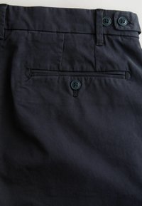 Dunkelblaue Hose mit glattem Stoff, einer Gesäßtasche mit Knopfverschluss und dezenten Nähten entlang des Bundes.