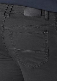 Schwarze Denim-Jeans haben eine glatte Textur, eine Gesäßtasche und ein Lederetikett am Bund. Das Design ist schmal geschnitten und weist dezente Nähte auf.