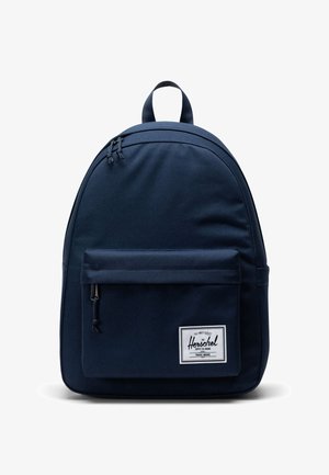 Meriini sininen kangaskotelo, jossa on kaareva siluetti, vetoketjullinen pääosasto, etutasku ja etupuolella brändättynimi.