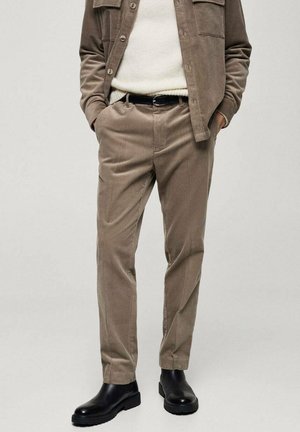 Pantaloni in velluto a coste beige con vestibilità dritta, dotati di tasche laterali, texture liscia e indossati con stivaletti neri alla caviglia.