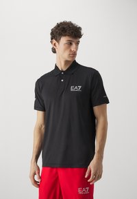 Schwarz lässiges Polohemd mit drei Knöpfen, kurzen Ärmeln und EA7-Logo auf der Brust. Hergestellt aus glattem Stoff, kombiniert mit roten Shorts.