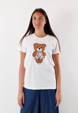 T-shirt bianca in cotone con un orso dei cartoni animati che indossa un vestito floreale. La maglietta ha un collo rotondo e maniche corte.