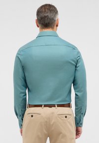 Turquoise langemouw shirt met een gestructureerd patroon, knoopmanchetten en een rechte kraag, gecombineerd met lichtbeige broek.
