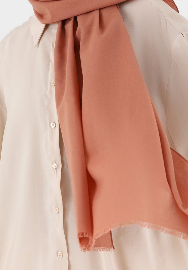 Chemise beige clair à boutons associée à une grande écharpe terracotta douce drapée autour du cou et des épaules.