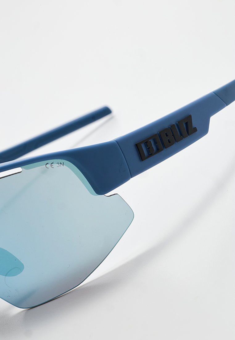 Blaue Sportsonnenbrille mit einer gewölbten Linse und seitlichen Blenden. Verfügt über schwarze Markenlogos am Bügel und eine matte Oberfläche im Rahmen.