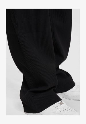 Svarte ribbede vide bukser med en jevn tekstur, som har en løs passform og avskåret nederkant, kombinert med hvite sneakers.
