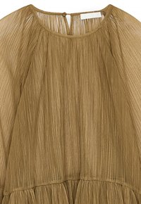 Top plisado de color verde oliva con escote redondeado, cierre de botón en la parte trasera y tela texturizada con detalles de diseño fluido.