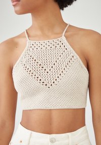 Szydełkowy top na halter w jasnym beżu z trójkątnym wzorem koronkowym i cienkimi ramiączkami, charakteryzujący się dopasowanym krojem i skróconym fasonem.