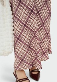 Jupe fluide à carreaux dans des nuances de prune et de crème avec une texture soyeuse. Associée à des chaussures bordeaux à bout pointu avec des accents de brides.