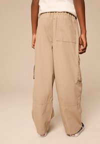 Pantaloni cargo in beige chiaro, con vestibilità rilassata, vita elastica, tasche a scomparsa e tasca laterale cargo. Tessuto morbido e resistente.