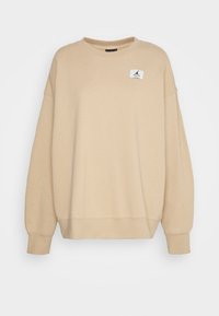 Felpa beige con scollatura rotonda, spalle scese, polsini a coste e una piccola etichetta nera del logo Jordan sul lato superiore sinistro del petto.