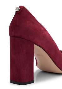 Escarpin en daim bordeaux, talon épais et bloc avec un accent argenté à l'arrière, texture lisse et design à bout arrondi.