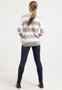 Pull à rayures grises et roses avec une coupe décontractée, associé à un jean skinny bleu foncé et des bottines noires, vu de dos.