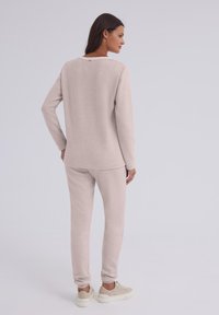 Jasnobeżowy zestaw odzieży domowej, składający się z bluzki z długim rękawem o okrągłym dekolcie oraz dopasowanych spodni. Miękka, fakturowana tkanina, casualowy krój.