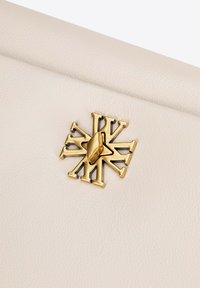 Pochette en cuir crème avec fermeture en métal doré au design d'éclat d'étoile, comprenant des formes entrelacées et un accent central proéminent.