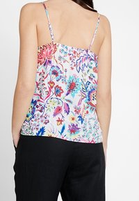 Camiseta sin mangas de estampado floral con tirantes ajustables, que presenta una parte trasera fruncida y colores vivos sobre un fondo claro.
