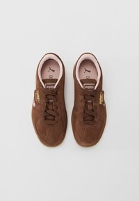 Bruna mockaskinns sneakers från Puma med rosa foder, svarta Puma-loggor inuti och gula "Puma Palermo"-etiketter på snörningen, visade ovanifrån.