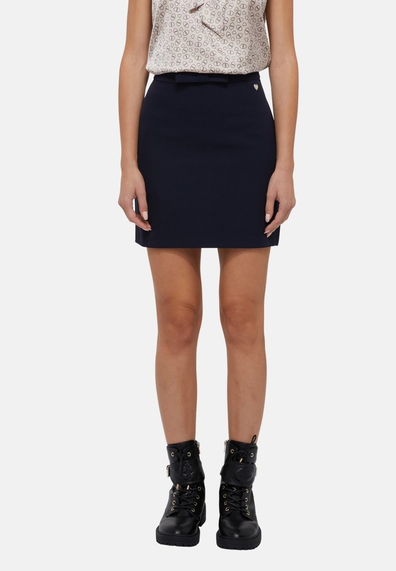 Mini-jupe bleu marine à coupe ajustée avec détail ceinture, associée à des bottines noires à lacets avec accents dorés et semelles robustes.