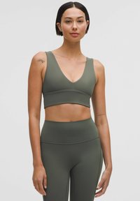 Olíva zöld sportmelltartó mély V-nyakkal, széles pántokkal és sima textúrával. Magas derekú, illeszkedő leggings-szel párosítva.