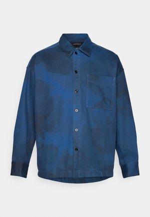 Oversized blauwe shirt met een waterdruppelpatroon, lange mouwen, knoopsluiting aan de voorkant, één borstzak en zwarte knopen.