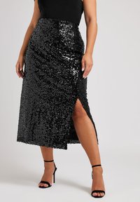 Svart midiklänning med paljetter, som har en sidöppning och en svepdesign, med en glansig yta. Matchas med svarta sandaler med remmar och hög klack.