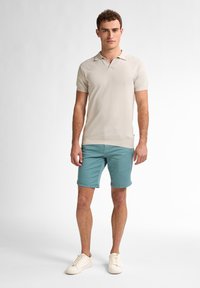 Beige, struktureret polo t-shirt med korte ærmer, parret med lys blå shorts og cremefarvede sneakers. Enkel design, ingen synlige mønstre.