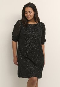 Robe en sequins noirs avec une coupe décontractée, col rond et manches bouffantes. La texture présente de nombreux sequins scintillants sur la surface.