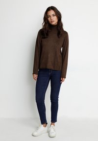 Pull à col roulé marron en tissu tricoté doux, associé à un jean skinny bleu marine et des baskets blanches. Manches longues, coupe décontractée.
