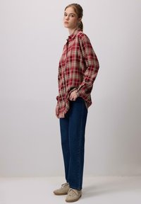 Punane ja beež ruuduline särk, millel on mugav lõige, koos tumehallide sirgete teksade ja beežide tossudega. Lihtne disain, ilma silmapaistvate mustriteta.