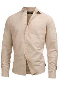 Camisa de manga larga beige hecha de tejido texturizado. Presenta un cierre frontal con botones, cuello puntiagudo y un bolsillo en el lado izquierdo del pecho.